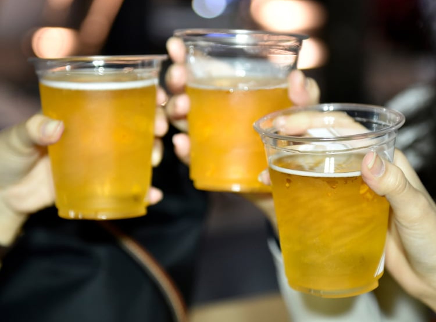 Image shows three hands holding three cups of beer