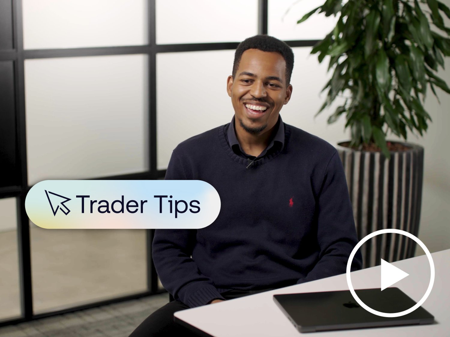 Man smiling in an office setting with a laptop on the desk, overlaid text reading "Trader Tips," and a play button icon indicating a video.