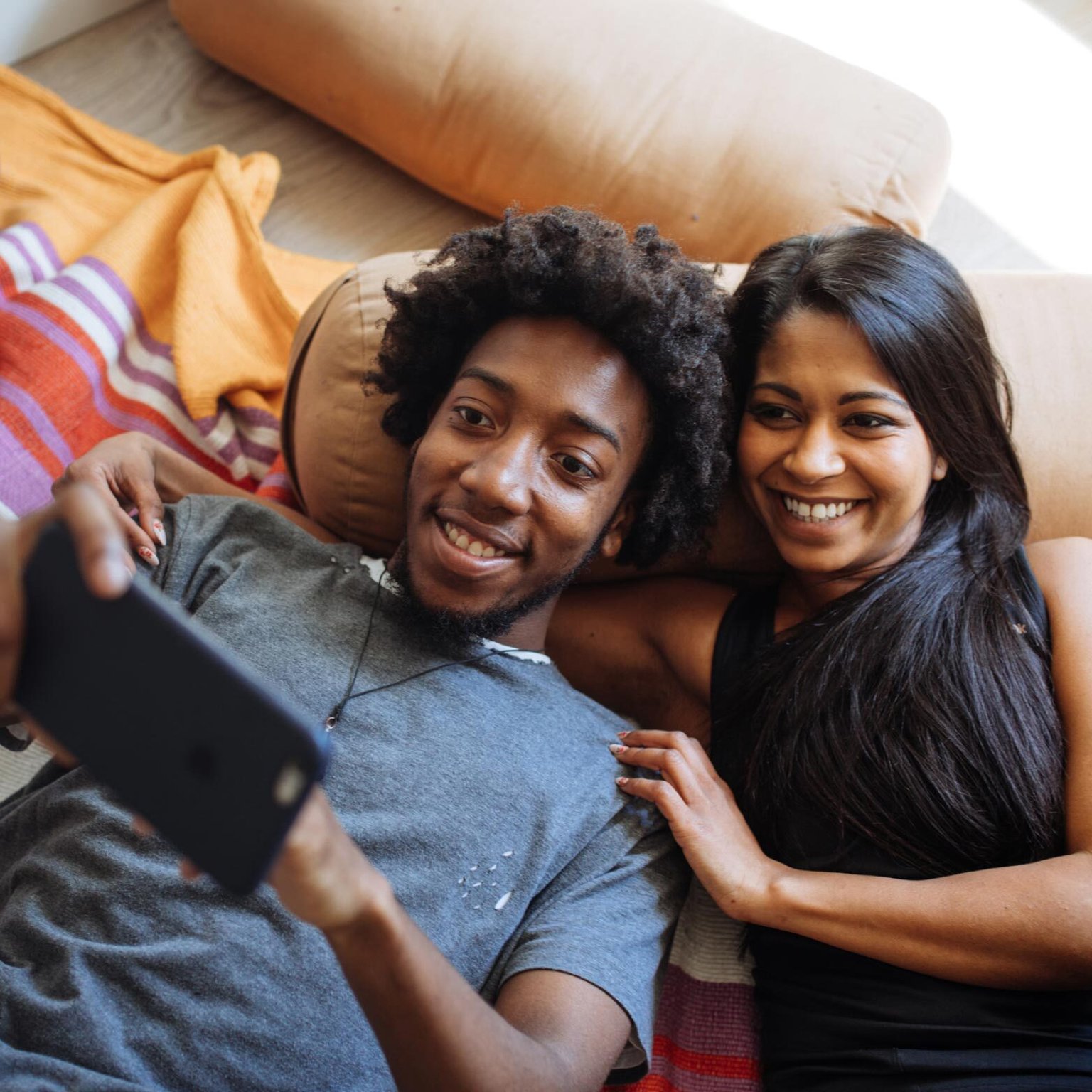 A happy couple lounging together, smiling while watching something on a smartphone