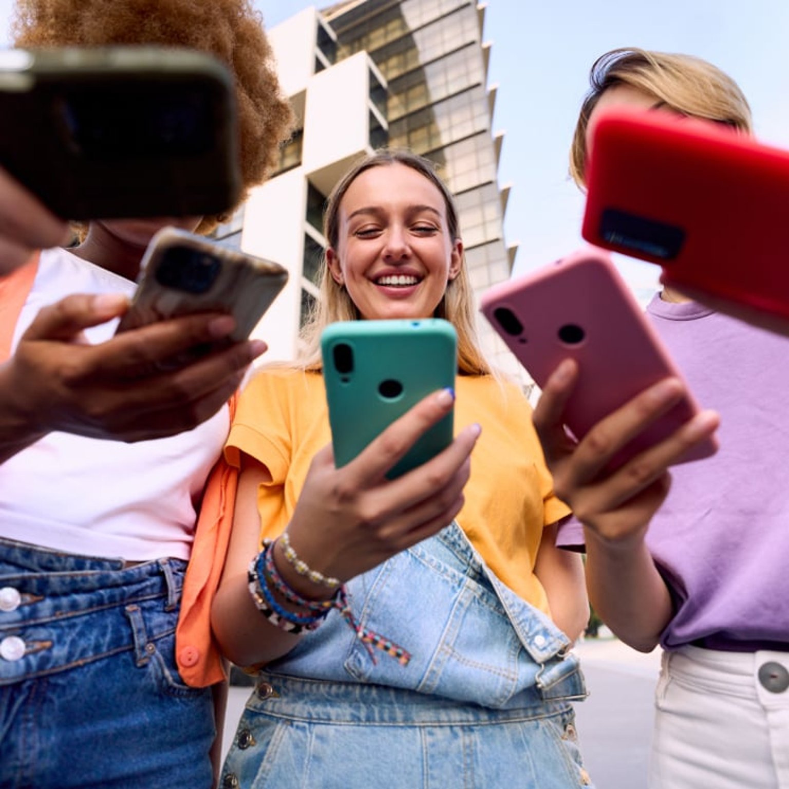 Group of young friends outdoors, smiling and engaging with their smartphones in a modern urban setting