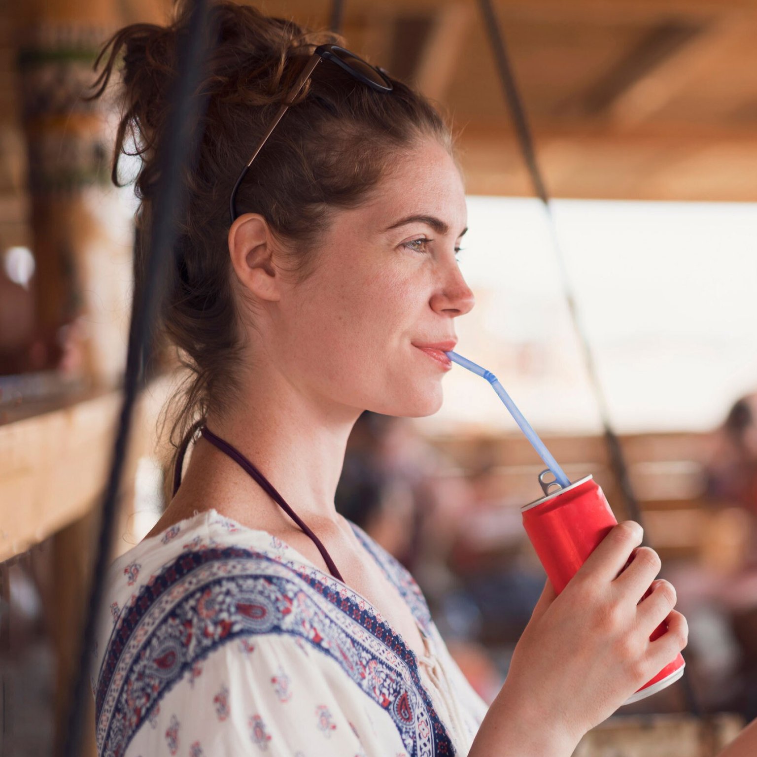 Woman standing and drinking out a red can from a blue straw