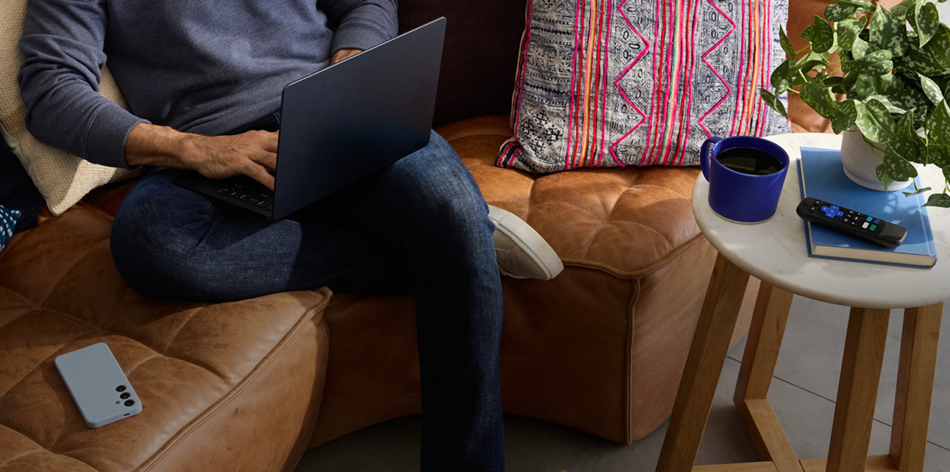 Man sitting on couch working on laptop with cell phone to his right