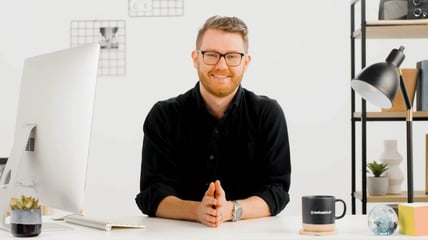 Image of a smiling man sitting at a desk with a computer, lamp and coffee cup that reads "The Trade Desk"