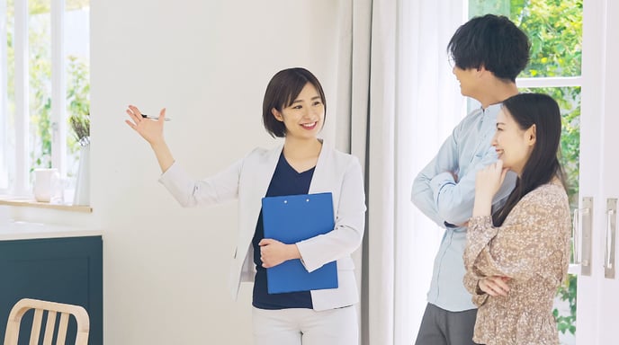 Couple with a real estate agent, holding a clip board and viewing a house.