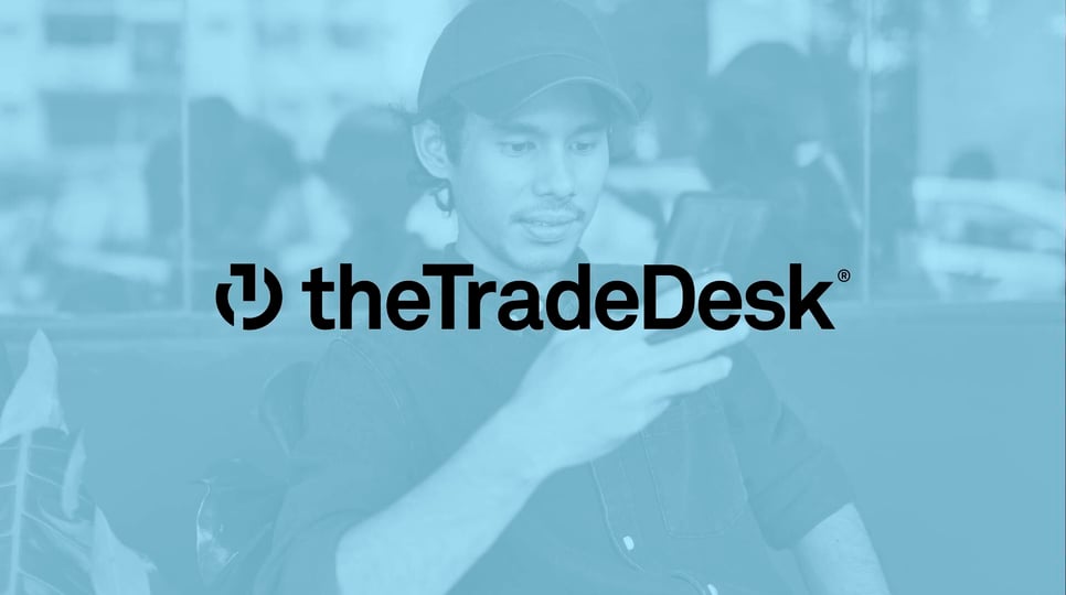 Man wearing a green hat, while staring at his phone with a blue cover and The Trade Desk logo in the center